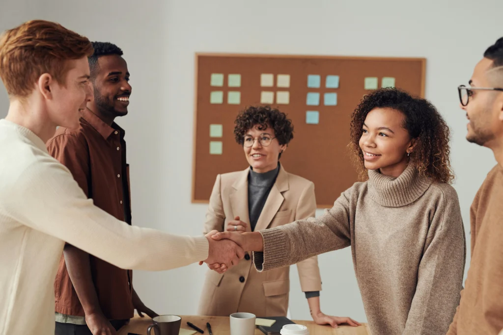 A man and a woman shake hands in front of other people in an office.