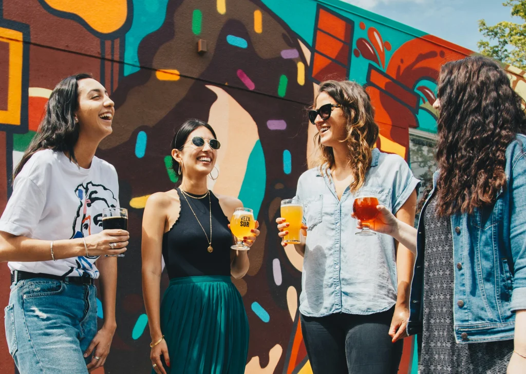 A group of friends laugh while holding drinks in their hands.
