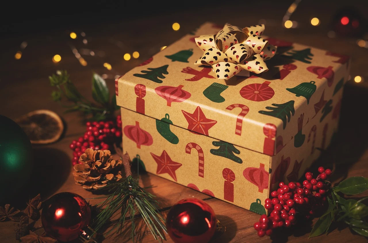 This image shows a gift box with Christmas prints surrounded by garland, mistletoe, string lights, and Christmas ornaments.