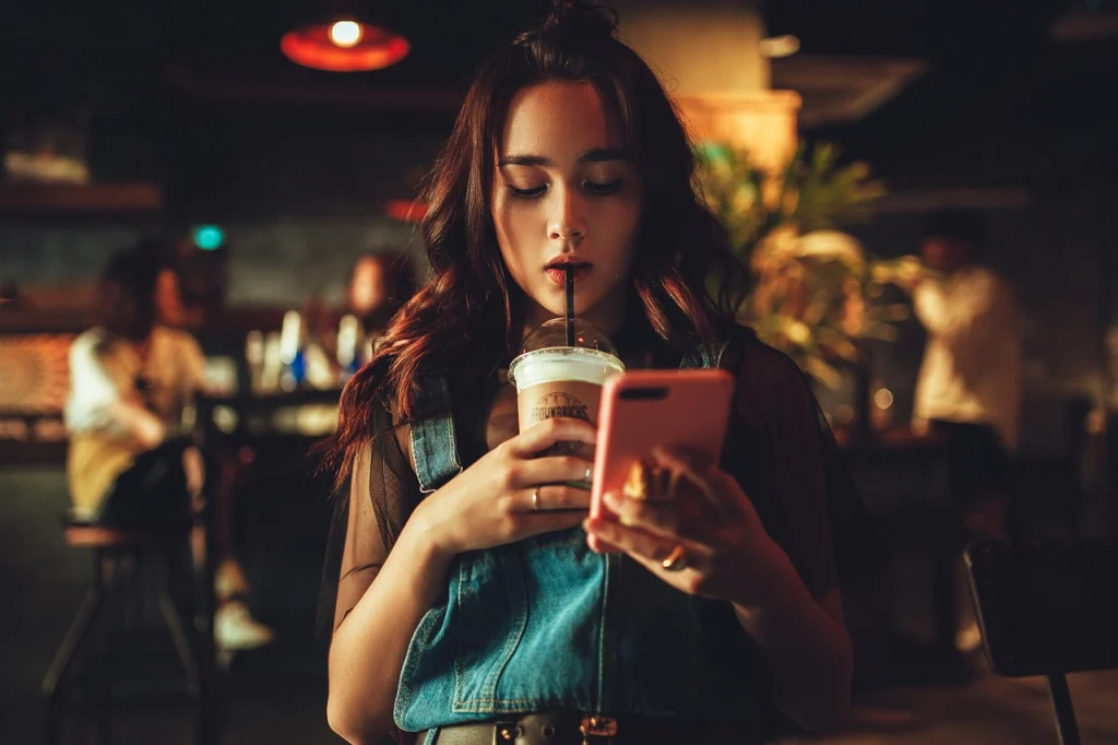 A woman stares at her phone while she sips on a drink.
