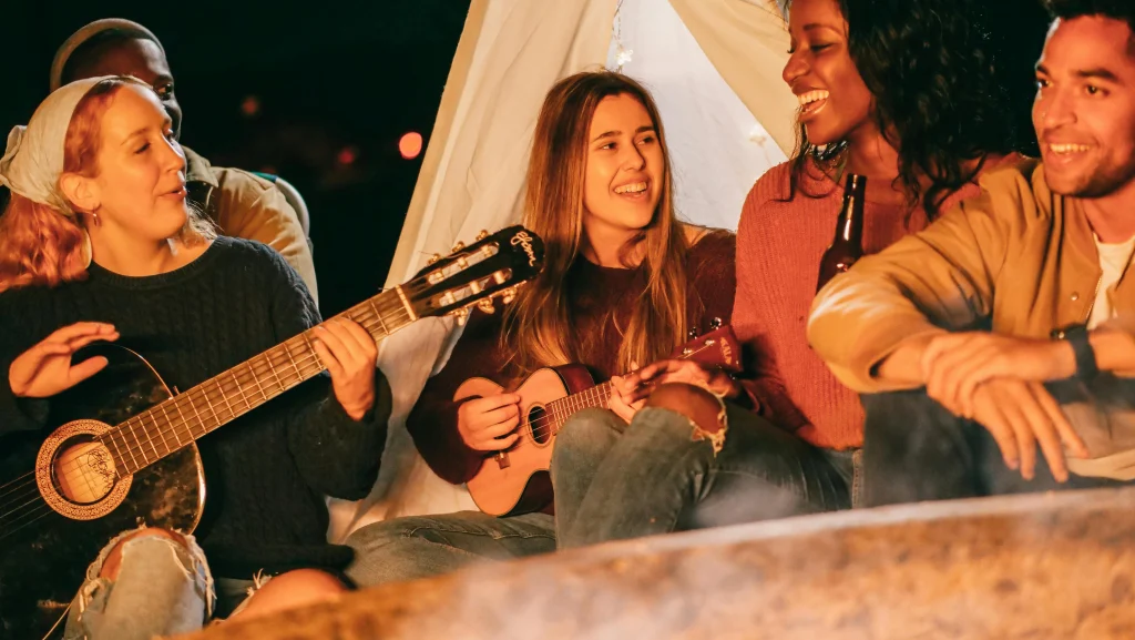 This image shows a group of people singing and playing guitar around a bonfire.
